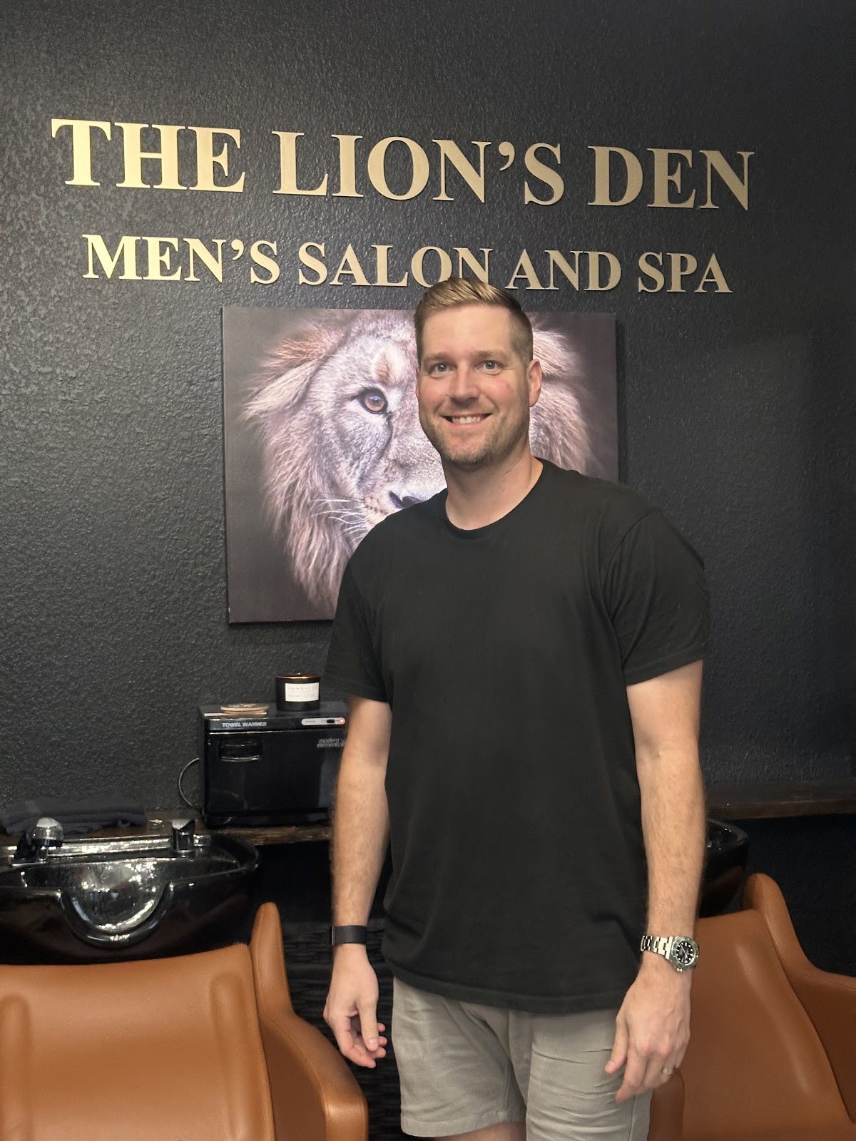 A happy client smiling in front of The Lion's Den signage