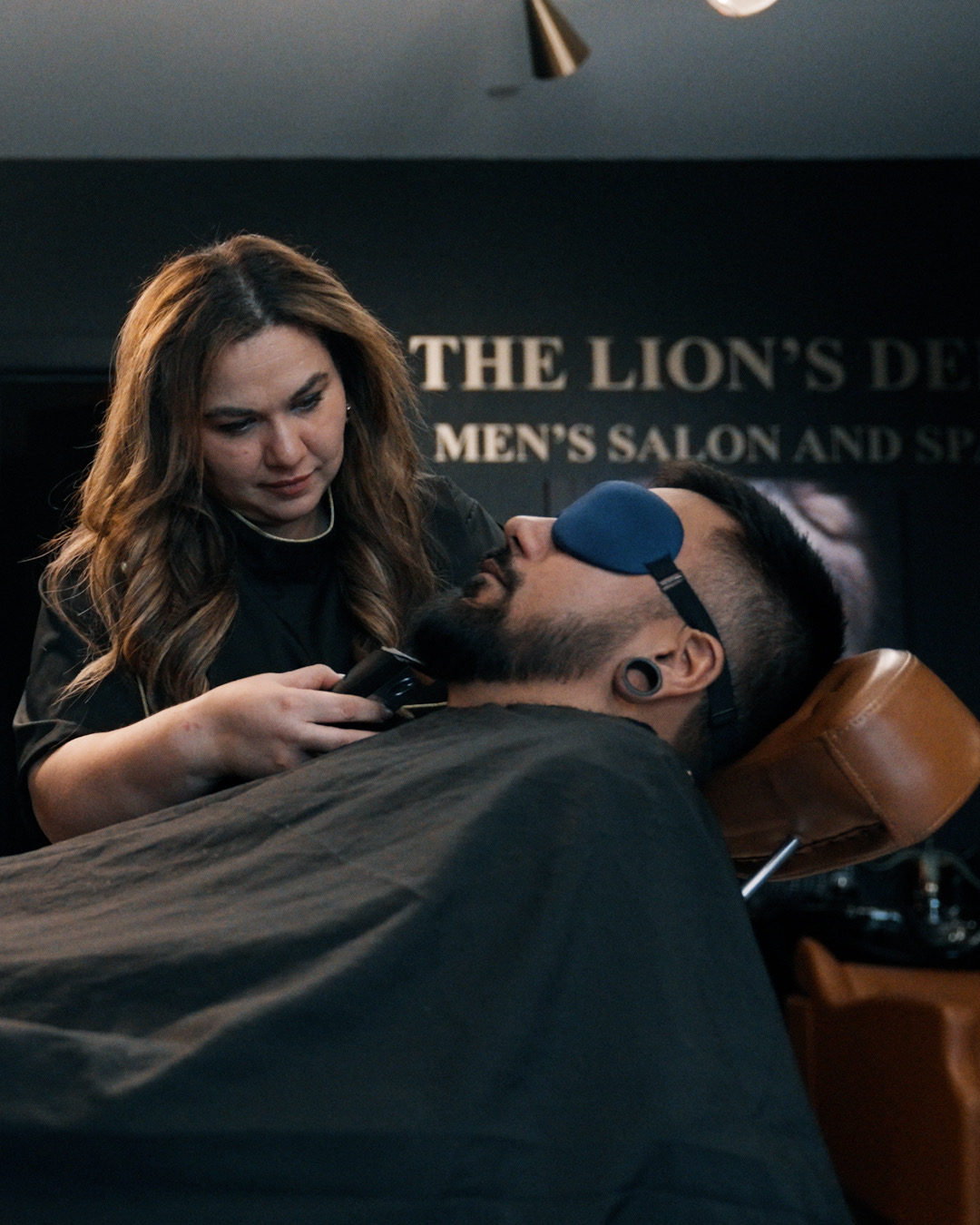 Blanca trimming a beard with precision while the client relaxes with an eye mask